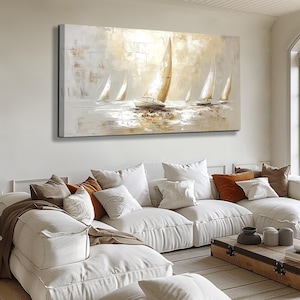 May include: An oil painting of sailboats on the water. The artwork uses a neutral colour palette with shades of white, beige, and brown. The sailboats have white sails, and the water reflects the light. The painting is displayed above a white sectional sofa.