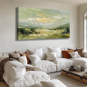 May include: An abstract landscape painting with a palette of greens, yellows, and whites. The artwork depicts rolling hills and a cloudy sky, creating a serene and natural scene. The painting is displayed above a white sectional sofa with various throw pillows.