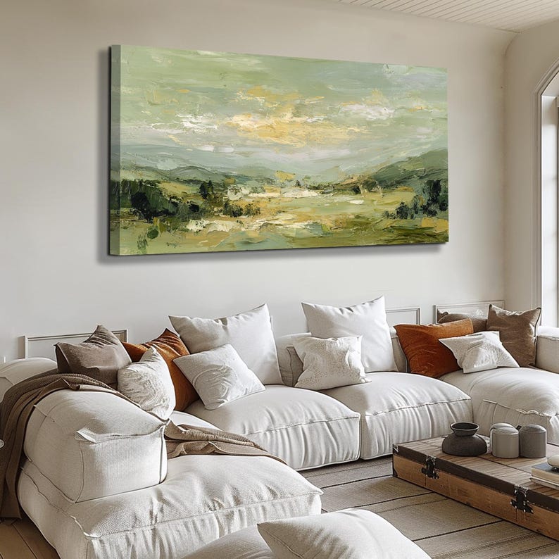 May include: An abstract landscape painting with a palette of greens, yellows, and whites. The artwork depicts rolling hills and a cloudy sky, creating a serene and natural scene. The painting is displayed above a white sectional sofa with various throw pillows.