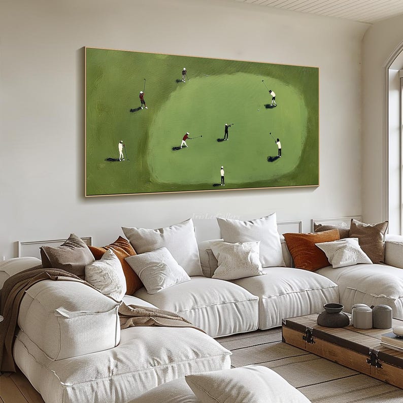 May include: A framed painting depicts a golf course scene with several small figures in white, red, and black attire. The figures are engaged in golfing activities on a green field, set against a neutral background. The artwork is displayed above a white sectional sofa.