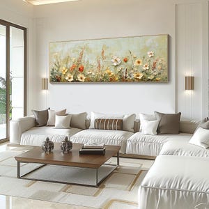 May include: A large rectangular floral painting with a gold frame hangs above a white sofa. The artwork features textured flowers in shades of yellow, orange, and white against a light green background. The room also includes a wooden coffee table and decorative pillows.