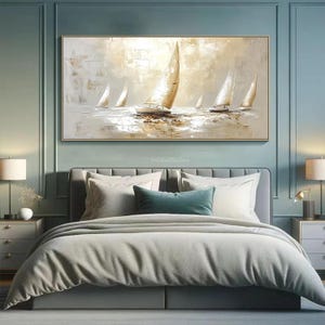 May include: An abstract oil painting depicting sailboats on water, in white, beige, and gold tones. The artwork is in a gold frame, above a bed with grey bedding and pillows. The theme is nautical and peaceful. The painting is a decorative item.
