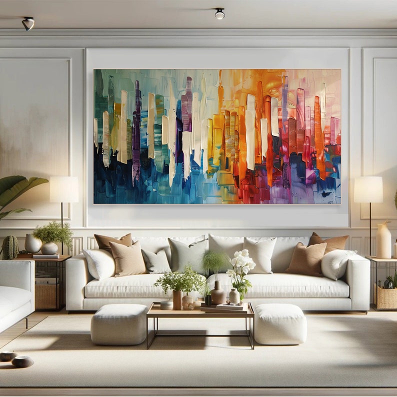 Puede incluir: Pintura abstracta de una ciudad con l&iacute;neas verticales de colores en tonos azules, morados, amarillos, naranjas y rojos. La pintura se exhibe en una pared blanca sobre un sof&aacute; blanco con almohadas y plantas.