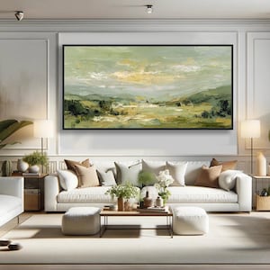 May include: An abstract landscape painting in a black frame. The artwork features a palette of greens, yellows, and blues, depicting a serene vista of hills and sky. The painting hangs above a white sofa with neutral-toned pillows.