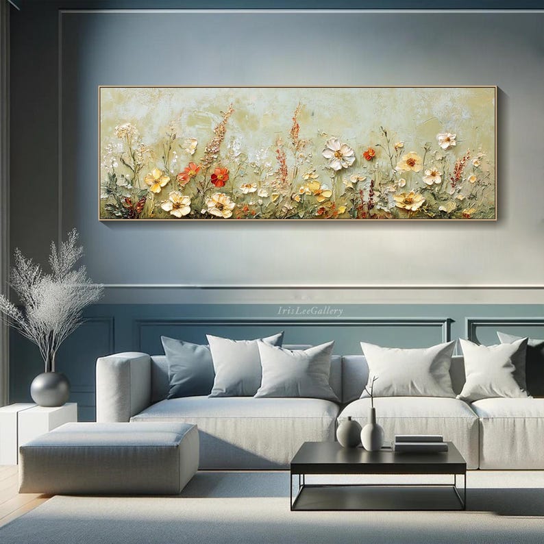 May include: A rectangular floral painting with a gold frame. The artwork features a textured, light green background with a variety of colorful flowers in shades of yellow, orange, and white. The painting is displayed above a gray sofa.