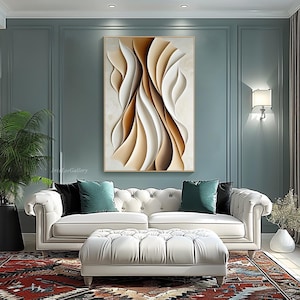 May include: Abstract wall art featuring a modern design with flowing lines and curves in shades of brown, beige, and white. The artwork is framed in a gold frame and is displayed on a wall in a living room setting.