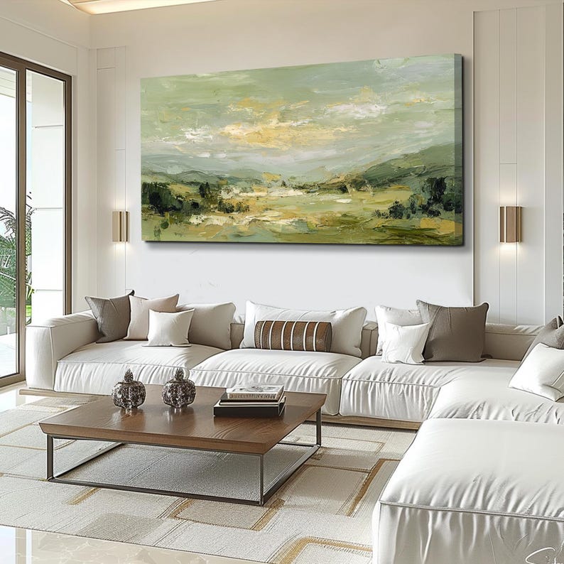 May include: An abstract landscape painting in shades of green, yellow, and white hangs above a white sectional sofa. The artwork depicts a serene scene of rolling hills and a cloudy sky. A wooden coffee table and decorative items complete the living room setting.