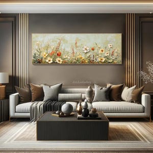 May include: A rectangular floral painting with a gold frame hangs above a sofa. The artwork features textured flowers in yellow, orange, and white against a light green background. The room has a modern design with a dark brown wall and a gray sofa.