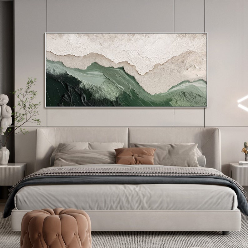 May include: Abstract landscape painting with green and white colors. The painting is framed and hanging on a wall above a bed with white bedding and brown pillows.