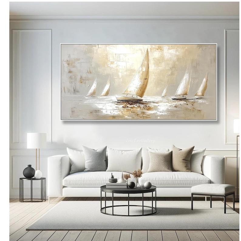 May include: An abstract oil painting of sailboats on water. The artwork uses a neutral palette of white, beige, and gold, with textured brushstrokes. The sailboats have white sails, and the water reflects the light. The painting is framed in a white rectangular frame.