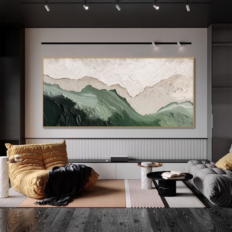 May include: Abstract landscape painting with green and white colors. The painting is framed in a thin gold frame and is hanging on a white wall in a modern living room.