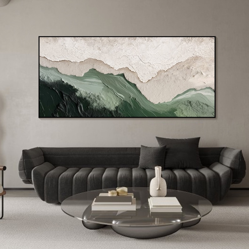 May include: Abstract landscape painting with green and white colors. The painting is framed and hanging on a wall above a gray sofa.