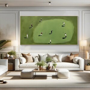 May include: A large rectangular framed painting depicts a golf course scene. Several small figures in white and red attire are playing golf on a green field. The artwork hangs above a white sofa with decorative pillows.