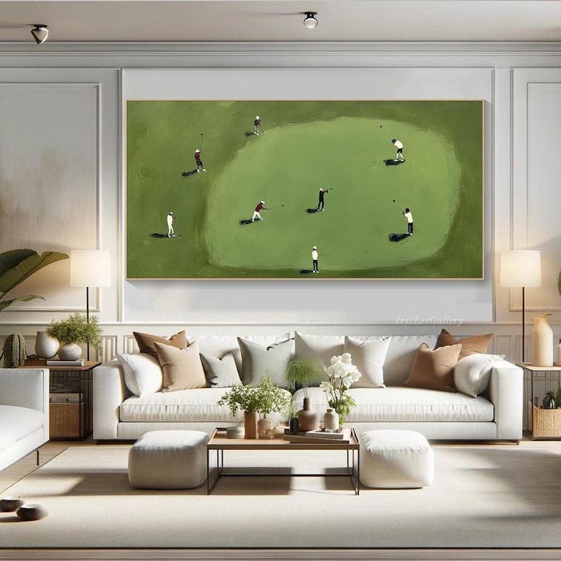 May include: A large rectangular framed painting depicts a golf course scene. Several small figures in white and red attire are playing golf on a green field. The artwork hangs above a white sofa with decorative pillows.