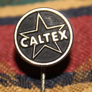 May include: A black and gold pin with a five-pointed star and the word "CALTEX" in white lettering.