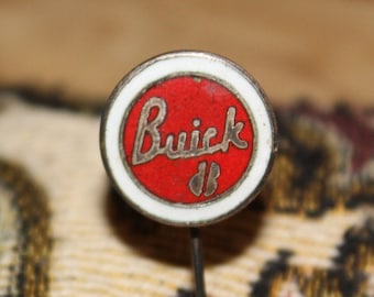 May include: A red and white enamel pin with the word "Buick" in silver lettering.