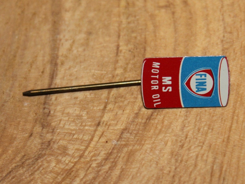 May include: A vintage FINA MS Motor Oil lapel pin. The pin features a rectangular design with a red and blue color scheme, and the text "MS MOTOR OIL" is printed vertically. The pin has a gold-colored metal pin.
