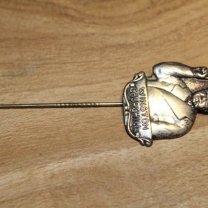 May include: Silver lapel pin featuring a sculpted image of Winston Churchill with the text "Winston Churchill" on the side. The pin has a long, thin, silver pin back.