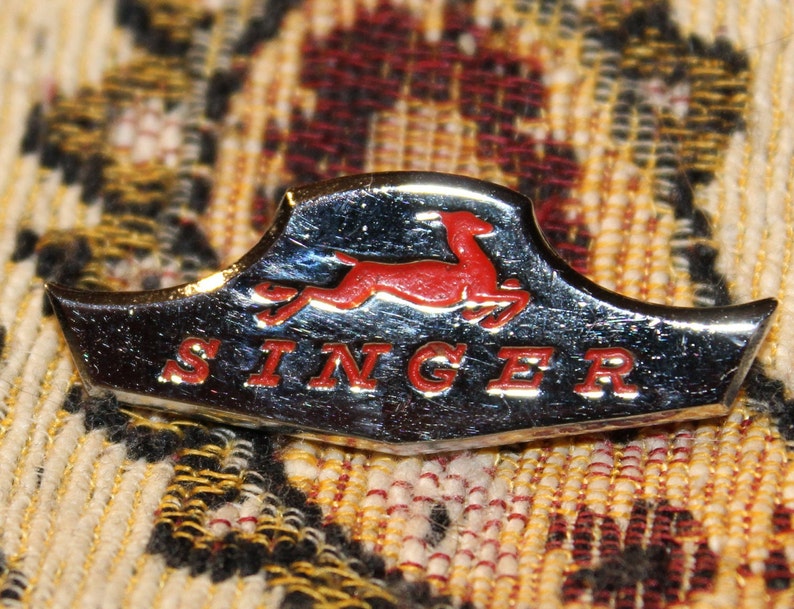 May include: A silver and red Singer sewing machine logo with a stylized running deer and the word "SINGER" in red letters.