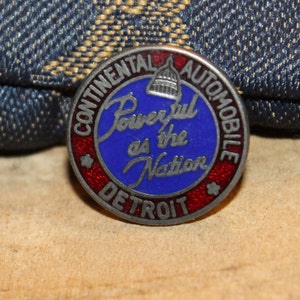 May include: A silver and red enamel pin with the words "Continental Automobile Detroit" and "Powerful as the Nation" around a blue enamel center with a white capitol building.