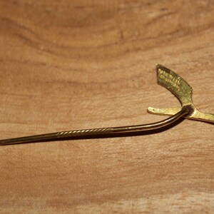 May include: A gold-colored pin with a twisted metal stem and a decorative, stylized bird design. The bird has a wingspan of approximately 2 inches.