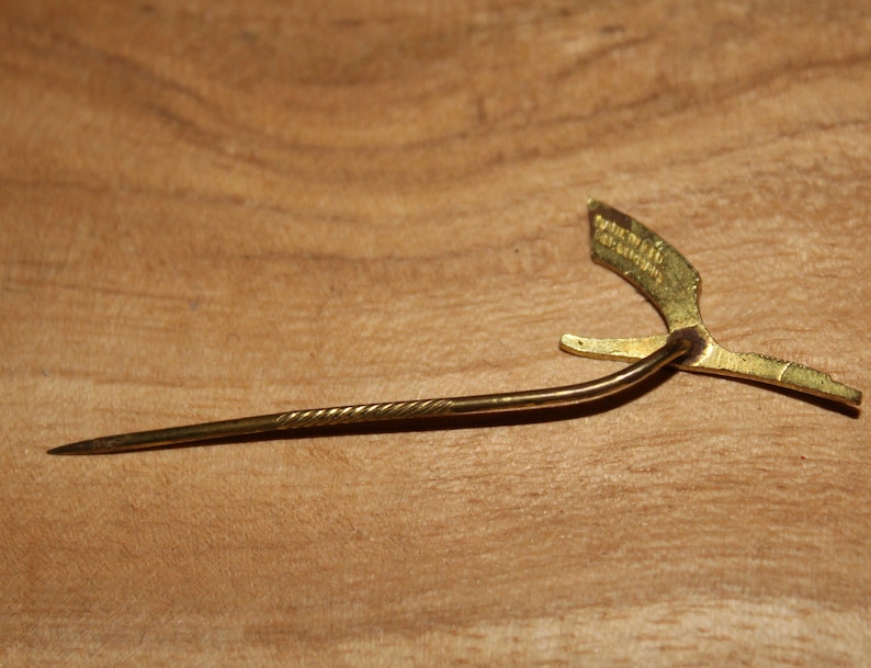 May include: A gold-colored pin with a twisted metal stem and a decorative, stylized bird design. The bird has a wingspan of approximately 2 inches.