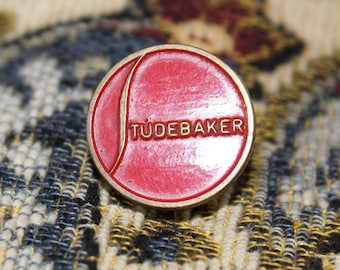 May include: A red and gold pin with the word "Studebaker" in gold lettering.