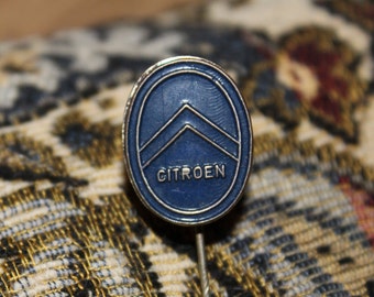 May include: A blue and silver metal pin with the word "CITROEN" in white letters. The pin features a stylized chevron design.