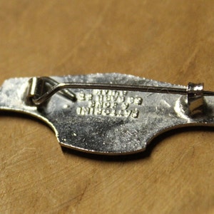 May include: Silver-toned metal pin with a bird design. The back of the pin has the text "BAYLORINI  BNDB 93  WYATT 93".
