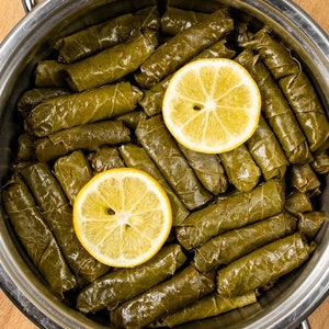 May include: A stainless steel pot filled with grape leaves stuffed with rice and herbs, topped with two lemon slices.