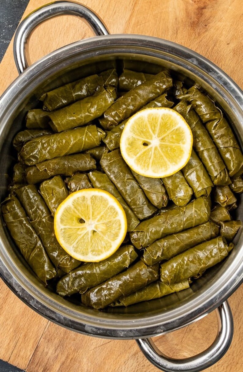 May include: A stainless steel pot filled with grape leaves stuffed with rice and herbs, topped with two lemon slices.