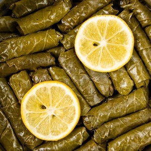 May include: A close-up of a plate of grape leaves stuffed with rice and herbs, topped with two lemon slices.