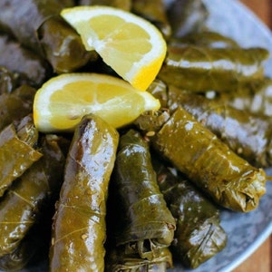 May include: A plate of grape leaves stuffed with rice and herbs, also known as dolmades, topped with lemon wedges.