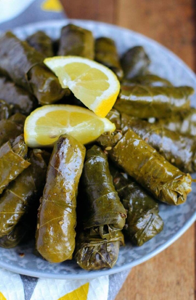 May include: A plate of grape leaves stuffed with rice and herbs, also known as dolmades, topped with lemon wedges.