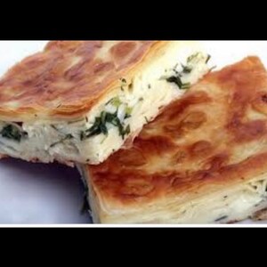May include: Two golden brown pastries filled with a white cheese and green herbs. The pastries are layered and flaky.