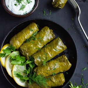 May include: A black skillet filled with grape leaves stuffed with rice and herbs. The grape leaves are arranged in a circular pattern. There is a small bowl of white sauce and a fork on the side.