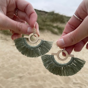 Puede incluir: Un par de pendientes de borla verde con un dise&ntilde;o de c&iacute;rculo y barra de madera. Los pendientes est&aacute;n hechos a mano y presentan una forma geom&eacute;trica &uacute;nica.