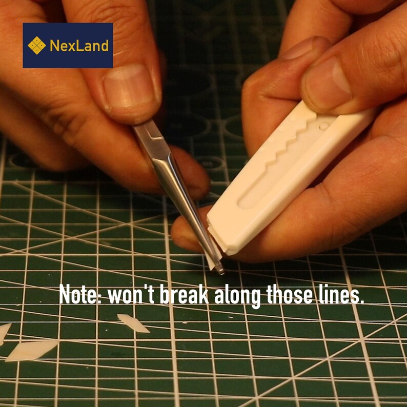 May include: A close-up of hands using a craft knife and a metal tool to cut a small piece of white material on a green cutting mat. The text "Note: won't break along those lines" is visible.