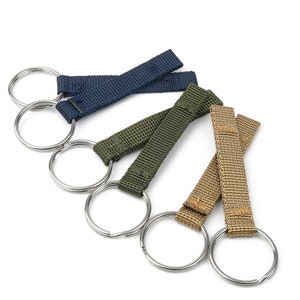 May include: Four keychains with different colored straps and silver rings. The straps are navy blue, green, and two beige straps.