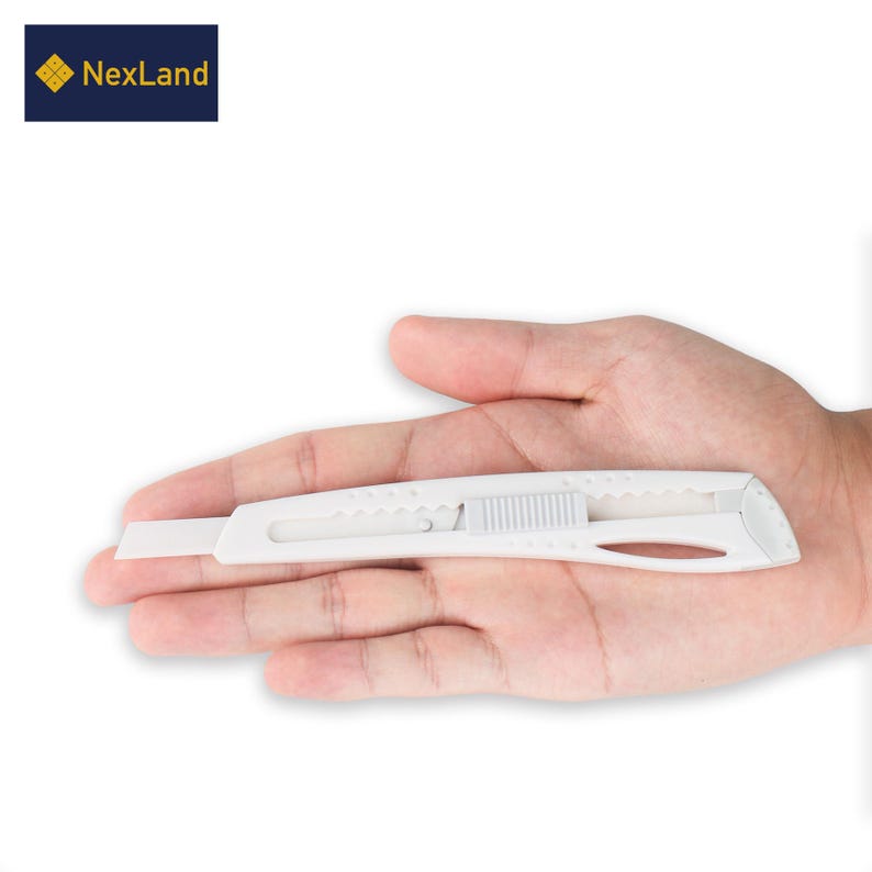 May include: A white utility knife with a retractable blade, held in a hand. The knife has a ridged slider and a curved handle. The NexLand logo is in the upper left corner.