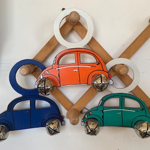 May include: Three wooden toy cars with bells hanging on a wooden rack. The cars are painted orange, blue, and green.