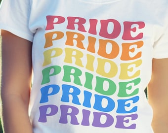 Puede incluir: Una camiseta blanca con la palabra "PRIDE" repetida seis veces en colores arcoíris. La palabra está en una fuente retro y redondeada.