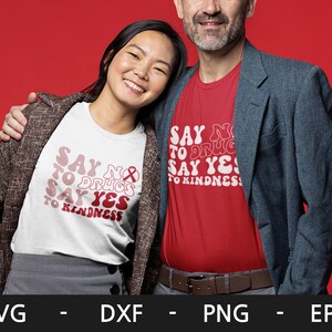 May include: Two people wearing t-shirts with the text "Say No to Drugs Say Yes to Kindness" in a retro font. The woman is wearing a white t-shirt and the man is wearing a red t-shirt.