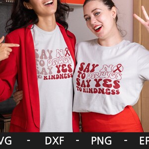 May include: Two women wearing white t-shirts with the text "Say No to Drugs Say Yes to Kindness" in red, retro-style lettering. The text is surrounded by a red ribbon.