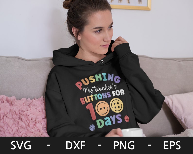 Pode incluir: Um moletom preto com o texto "PUSHING My teacher's BUTTONS FOR 100 Days" em cores do arco-&iacute;ris com bot&otilde;es coloridos ao redor do texto.