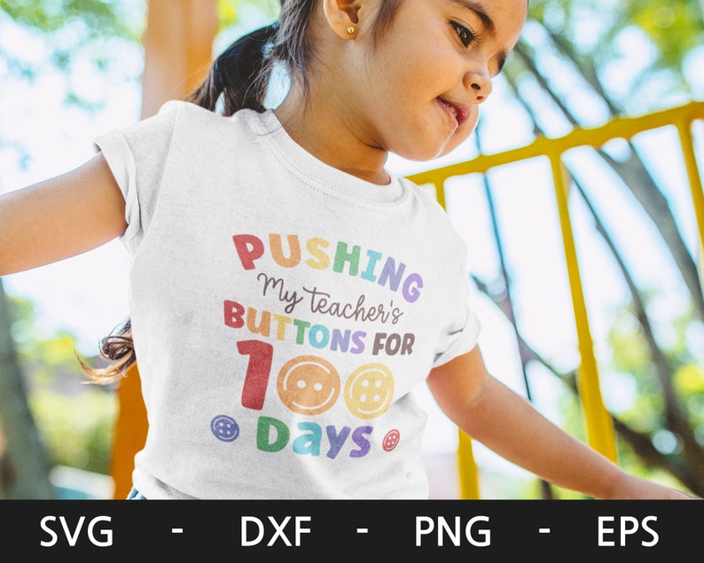 Pode incluir: Uma camiseta branca com o texto "Pushing my teacher's buttons for 100 days" em cores do arco-&iacute;ris com designs de bot&otilde;es.
