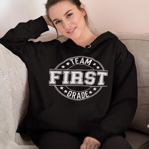 May include: Black hooded sweatshirt with a white circle graphic that says "Team First Grade" with stars around the circle.