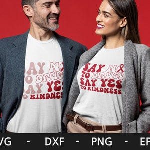 May include: Two people wearing white t-shirts with red text that says "Say No to Drugs Say Yes to Kindness". The text is in a retro font style. The people are wearing casual clothing and are standing against a red background.