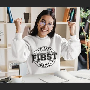 May include: A white sweatshirt with a black circle graphic that says "Team First Grade" in a vintage style font.