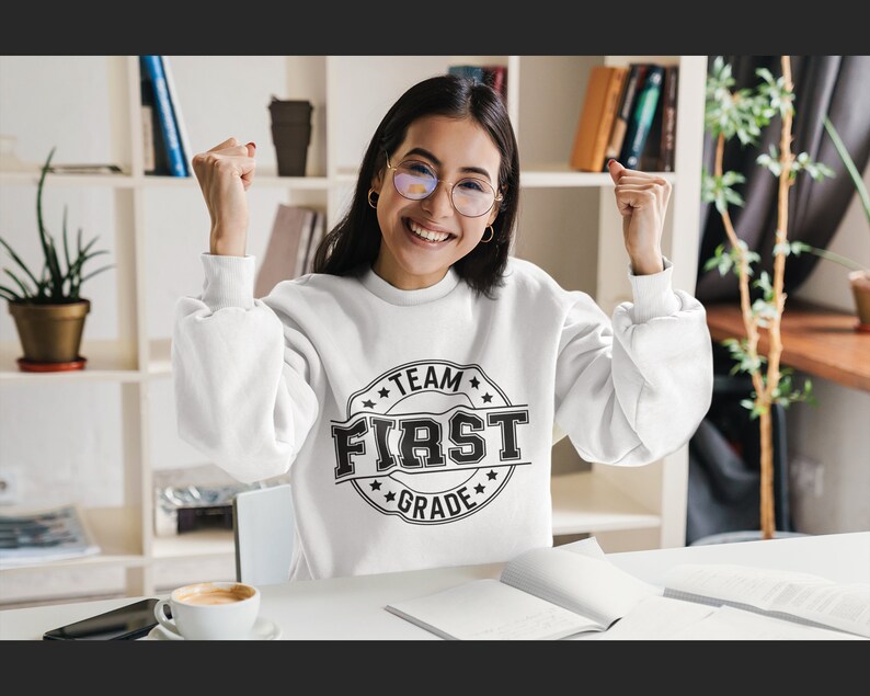 May include: A white sweatshirt with a black circle graphic that says "Team First Grade" in a vintage style font.